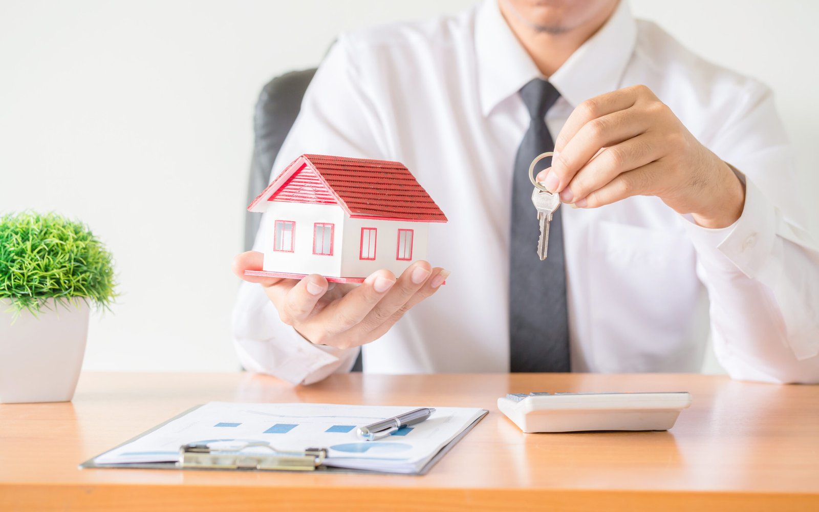Manos protegiendo una casa y sus llaves como símbolo de asesoría inmobiliaria